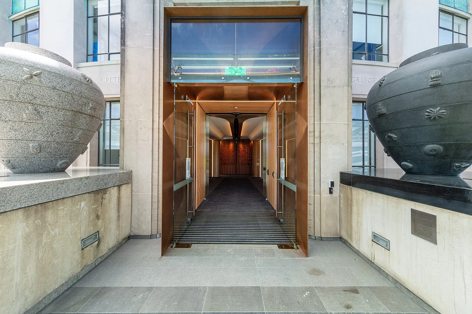 A doorway of Auckland Museum framed in copper-coloured metal, with a large carved stone vessel on either side