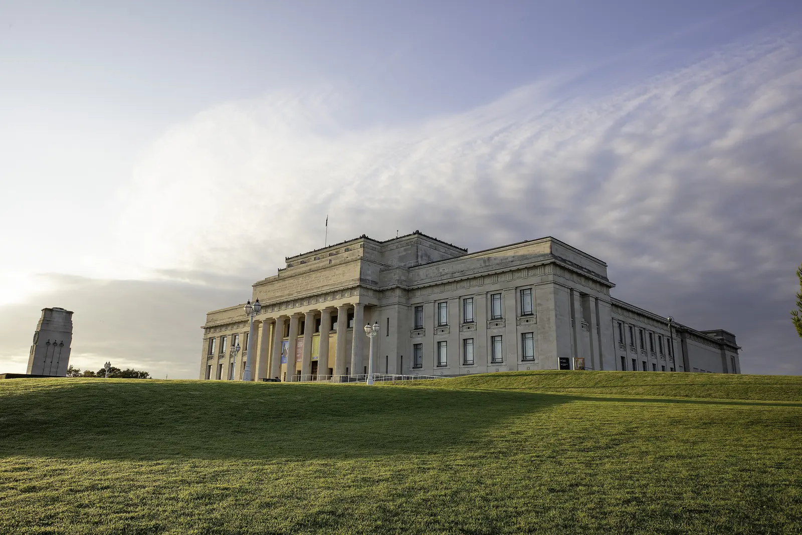 Auckland War Memorial Museum on its grassy hill at dusk, with the columned portico lit by low sun and the cenotaph tower at left